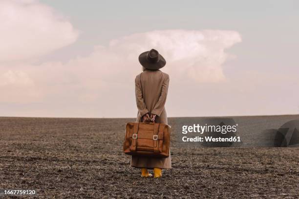 woman with brown suitcase standing in plowed field - brown hat imagens e fotografias de stock