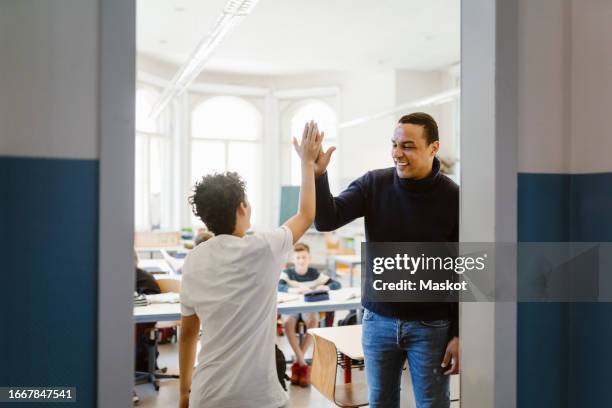 happy male teacher giving high-five to schoolboy standing in classroom - male teacher in a classroom stock-fotos und bilder