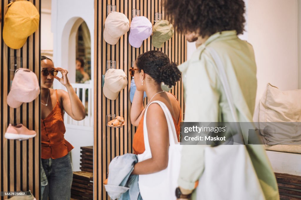 Woman trying sunglasses while standing by man at fashion boutique