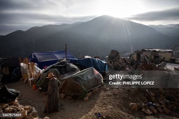An earthquake survivor walks near tents used as makeshift shelters, as the sun rises over the Atlas mountains in the village of Moulay Brahim in the...