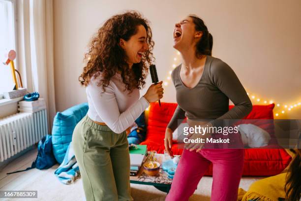 playful young women enjoying music while singing at home - hair brush stock pictures, royalty-free photos & images