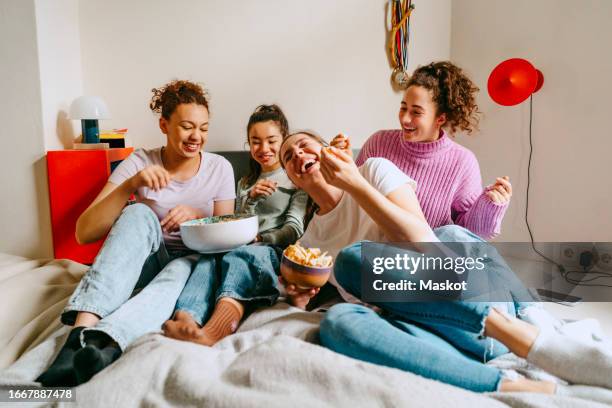 cheerful female friends watching tv while enjoying snacks at home - snack stock pictures, royalty-free photos & images