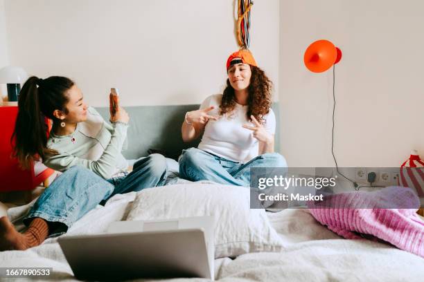 young woman photographing female friend through smart phone at home - pillow icon stock pictures, royalty-free photos & images