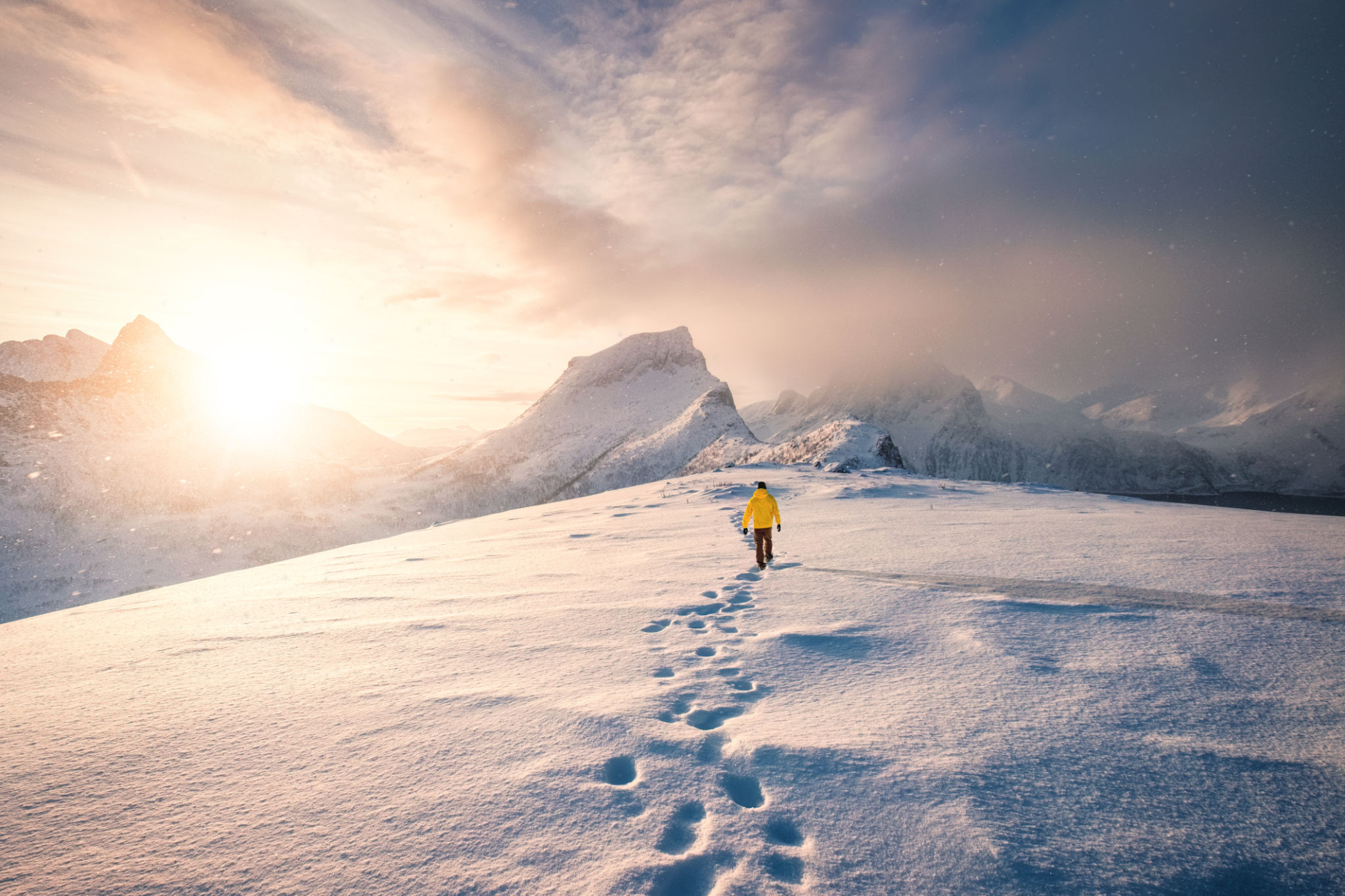 Mountaineer walking with footprint in snow storm and sunrise over snowy mountain in Senja Island Mountaineer walking with footprint in snow storm and sunrise over snowy mountain in Senja Island
