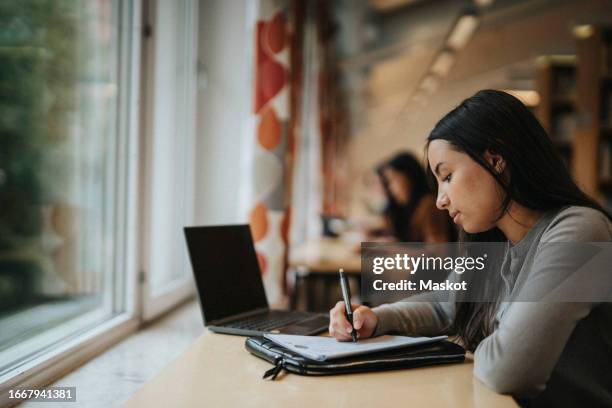 side view of student writing in paper while studying in library - arabic writing stock pictures, royalty-free photos & images