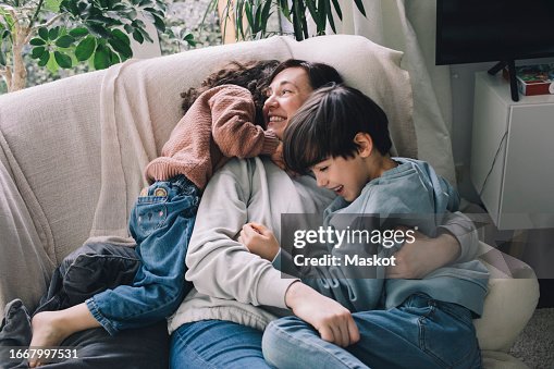 Playful boy and girl with mother on sofa at home Playful boy and girl with mother on sofa at home