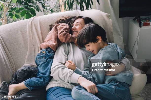 playful boy and girl with mother on sofa at home - levensstijl stockfoto's en -beelden