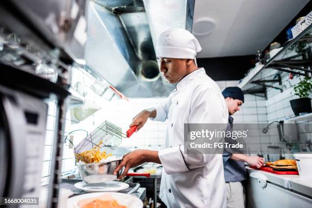 koch junger mann, der pommes frites in einer großküche zubereitet - kochberuf stock-fotos und bilder