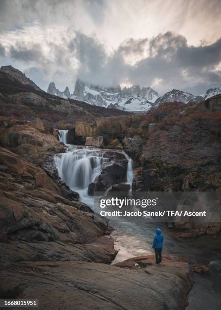 hiker stands on bluff above waterfall - chile torres del paine stock pictures, royalty-free photos & images