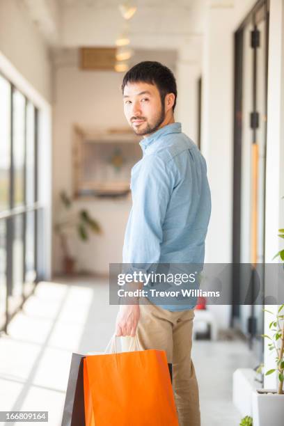 casually dressed man holding shopping bags - looking over shoulder stock-fotos und bilder