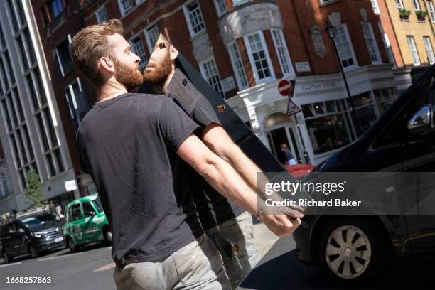Delivery workman very carefully carries a fragile mirror along a street in central London, on 14th September 2023, in London, England.