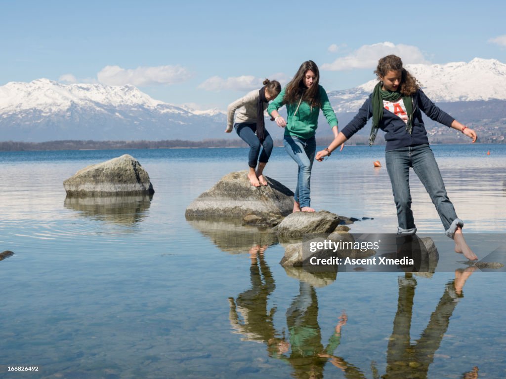Teen girls balance on stepping stones, mtn lake