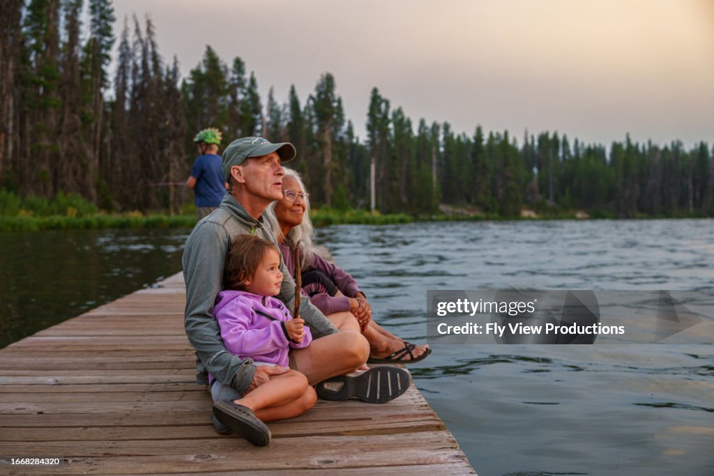 Grandparents and granddaughter enjoy sunset on a lake dock