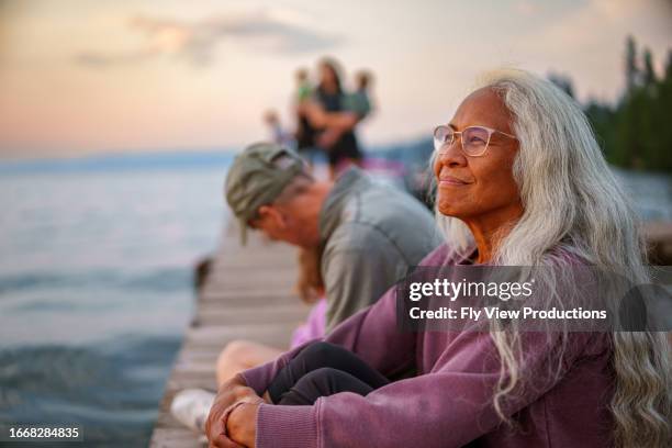 beautiful hawaiian senior woman enjoying sunset view from lake dock - woman pier stock pictures, royalty-free photos & images
