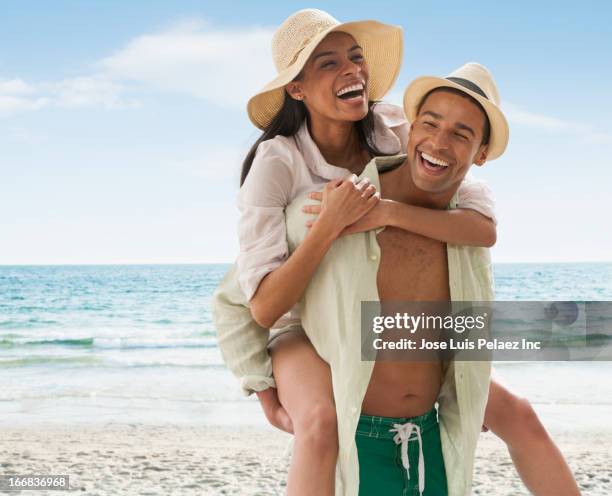 smiling man carrying girlfriend on beach - beach hut stock-fotos und bilder