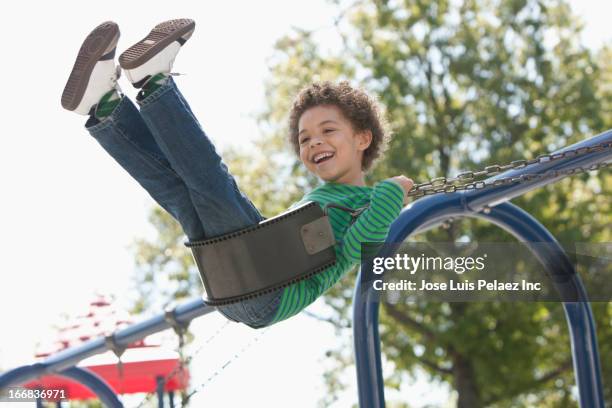 mixed race boy playing on swing at park - west new york new jersey stock-fotos und bilder