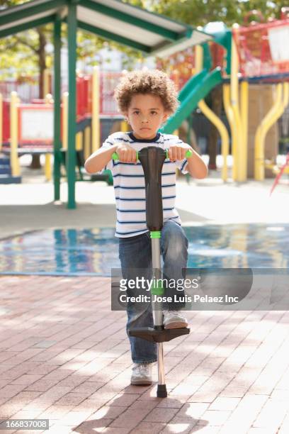 mixed race boy holding pogo stick at playground - pogo stock-fotos und bilder