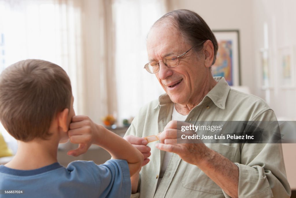 Older Caucasian man putting bandage on grandson