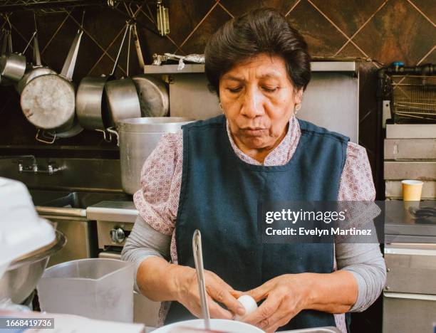 an older mexican woman peeling an egg in a restaurant-market kitchen - yonkers fotografías e imágenes de stock