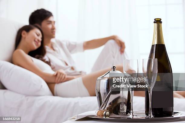 young couple sitting on bed - champagner gläser mit flasche unscharfer hintergrund stock-fotos und bilder