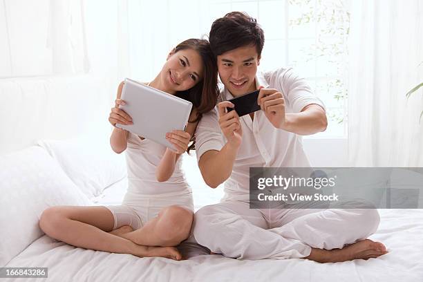 young couple holding mobile phone and tablet computor on bed - computor bildbanksfoton och bilder