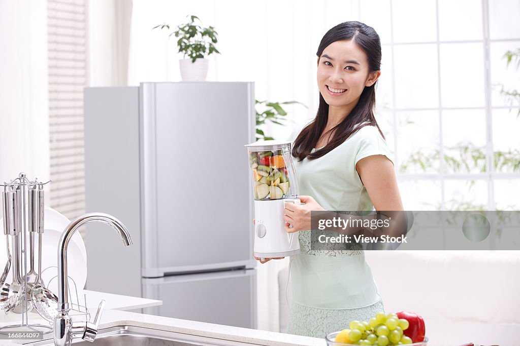 Young woman holding blender in kitchen