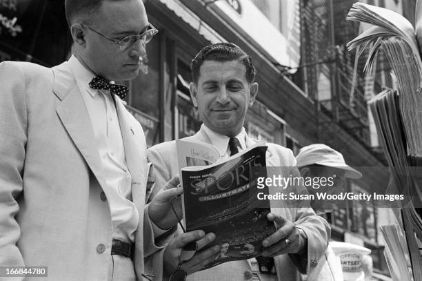 Pair of men look through the premiere issue of Sports Illustrated magazine on a Manhattan sidewalk, New York, New York, August 16, 1954.
