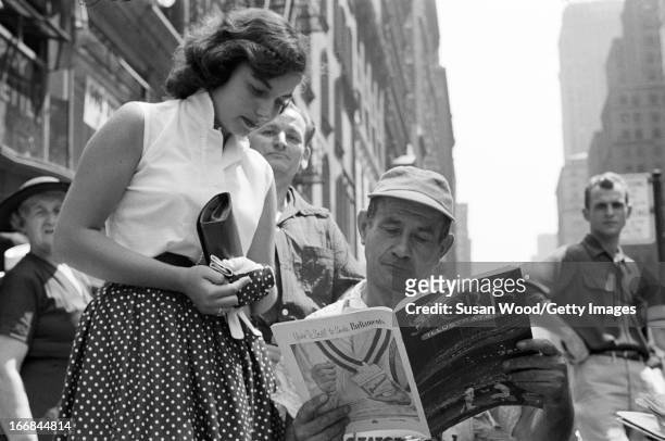News vendor looks through the premiere issue of Sports Illustrated magazine on a Manhattan sidewalk as onlookers read over his shoulder, New York,...