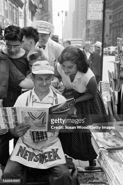 News vendor looks through the premiere issue of Sports Illustrated magazine on a Manhattan sidewalk as onlookers read over his shoulder, New York,...