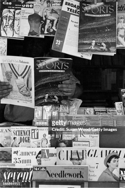 News vendor looks through the premiere issue of Sports Illustrated magazine in his stand, New York, New York, August 16, 1954.