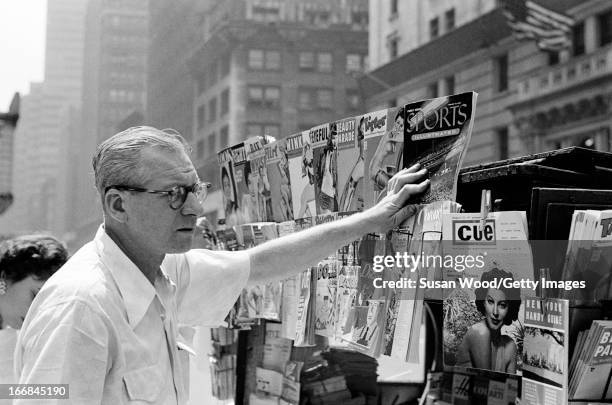 Man reaches for the premiere issue of Sports Illustrated magazine at a newsstand on a Manhattan sidewalk, New York, New York, August 16, 1954.