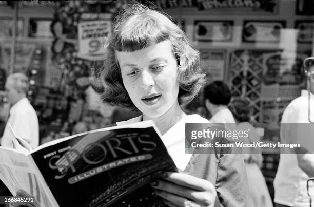 Woman looks through the premiere issue of Sports Illustrated magazine on a Manhattan sidewalk, New York, New York, August 16, 1954.