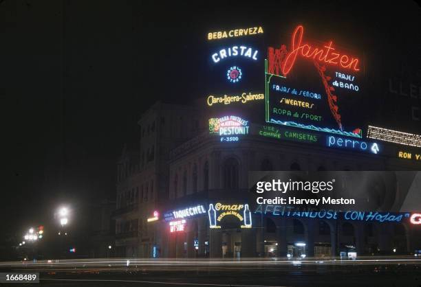 View of neon signs advertising liquor and clothing brands at night in Havana, Cuba, 1960s.
