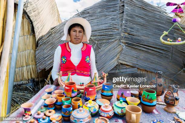 portrait of young peruvian woman in typical dress looking at camera standing at her small shop in uros floating islands over straw houses. aymara indigenous people. - floating island stock pictures, royalty-free photos & images