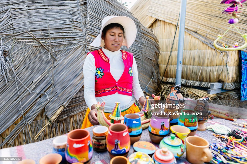Portrait of young Peruvian woman in typical dress looking standing at her small shop in Uros floating islands over straw houses. Aymara indigenous people.