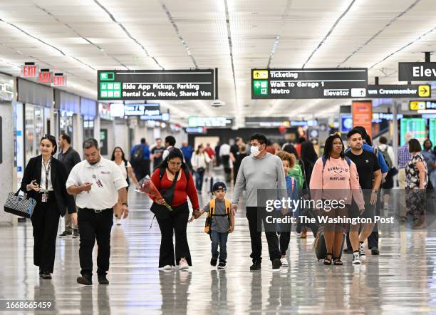 Folks, some wearing face masks to protect from the recent uptick in Covid cases, walk through the baggage area at Dulles International Airport on...