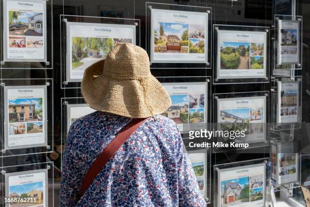 Woman looking at houses for sale in an estate agents window on 13th September 2023 in Cirencester, United Kingdom. Cirencester is known for having a...