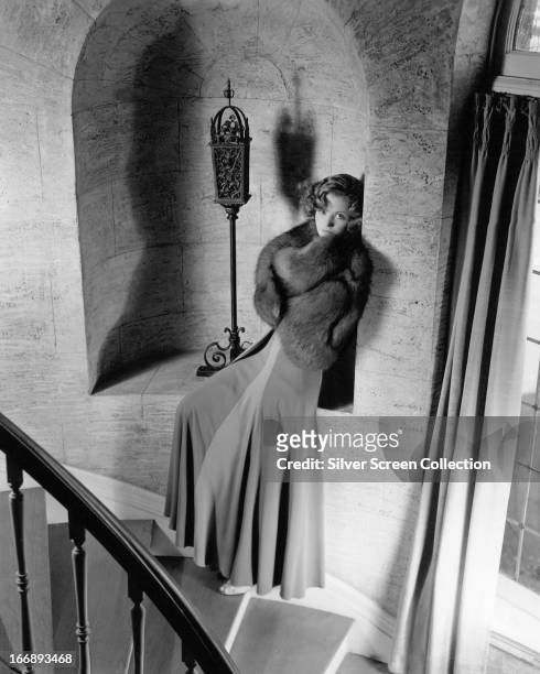 French actress Simone Simon wearing fur and posing on a spiral staircase, circa 1940.