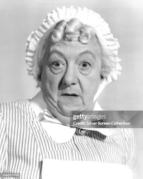 English actress Margaret Rutherford wearing a maid's housecoat and bonnet, circa 1960.