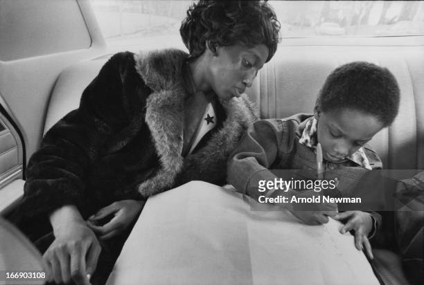 View of Ruthie Scott as she looks over her son's shoulder while he writes in the back of a car, Mansfield, Ohio, 1976.