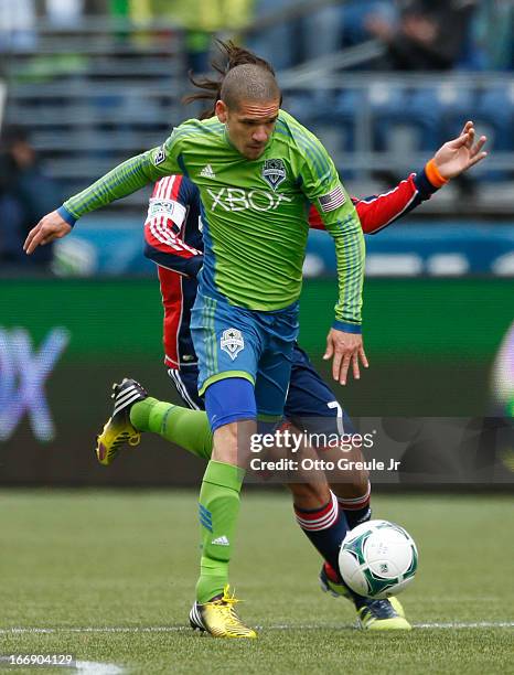 Osvaldo Alonso of the Seattle Sounders FC dribbles against Juan Toja of the New England Revolution at CenturyLink Field on April 13, 2013 in Seattle,...