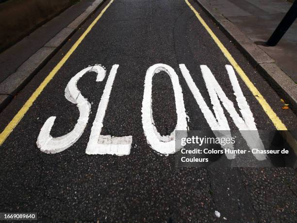 "slow" painted in white on the tarmac of a street in london, england, united kingdom - langzaam stockfoto's en -beelden