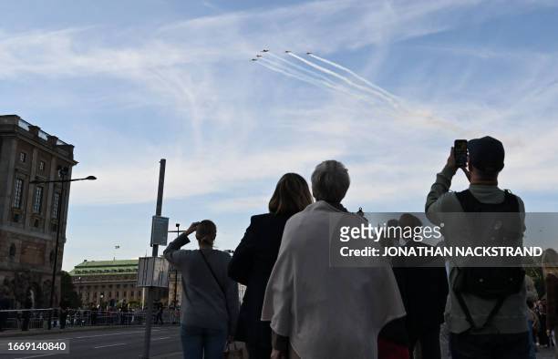 Spectators watch jet fighters flying in formation above the Royal Palace during festivities to celebrate the 50th anniversary of Sweden's King Carl...