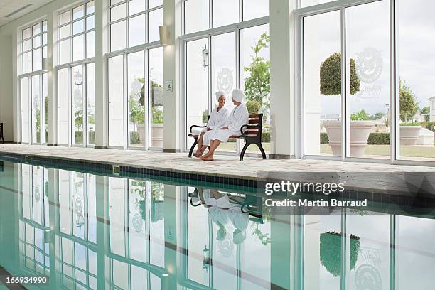 mujeres en batas de baño, sentado en el banco junto a la piscina del spa - balneario fotografías e imágenes de stock