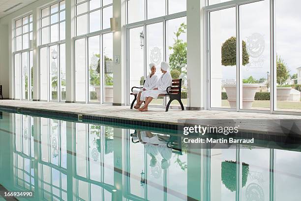 women in bathrobes sitting on bench poolside at spa - hälsosalong bildbanksfoton och bilder