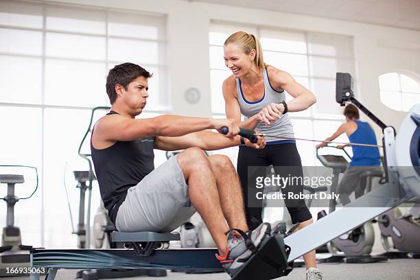 personal trainer with man on rowing machine in gymnasium - personlig tränare bildbanksfoton och bilder