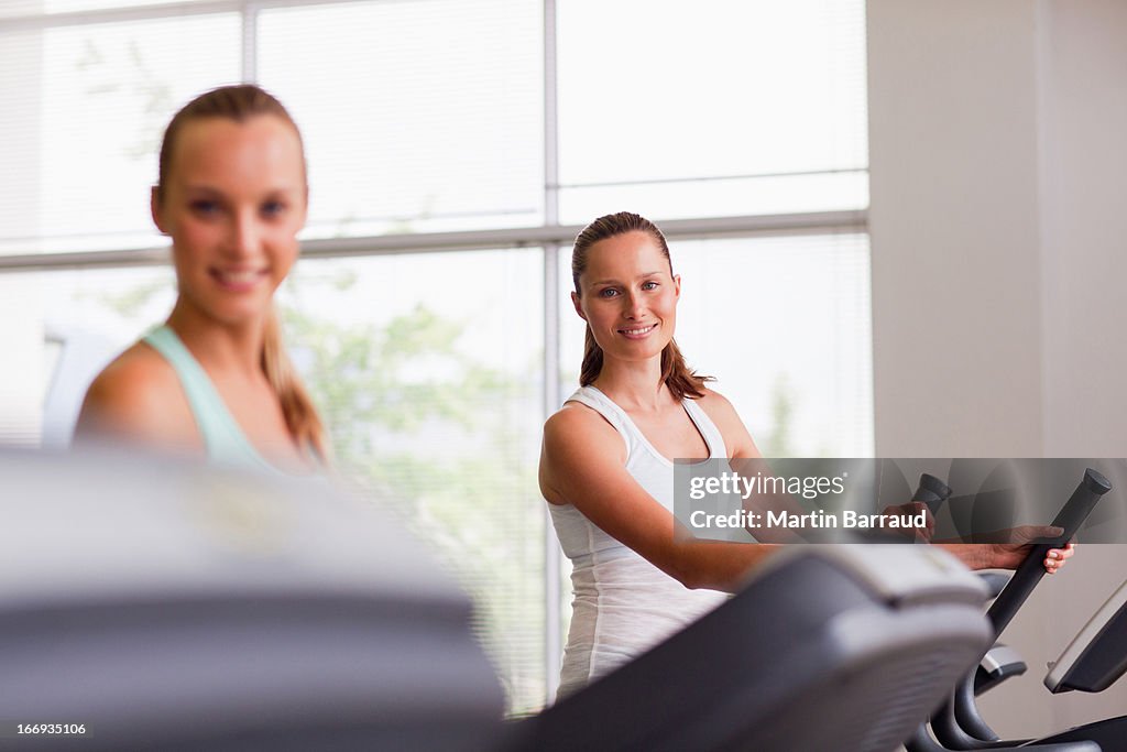 Smiling women using exercise equipment in gymnasium