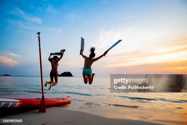 asian athletic woman with paddle board with friend on beach sunset. travel on summer holiday thailand. - pattaya stock pictures, royalty-free photos & images