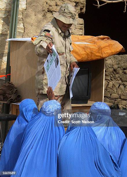 Army Psychological Operations 1st Sgt. Cesar Patriz of Brownsville, Texas hands out U.S. Army printed newsletters to burqa-clad Afghan women December...