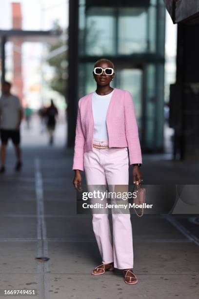 Fashion Week guest is seen wearing big sunglasses with a white frame, golden earrings, a pink jacket, underneath a white top, a jeans in rose with a...